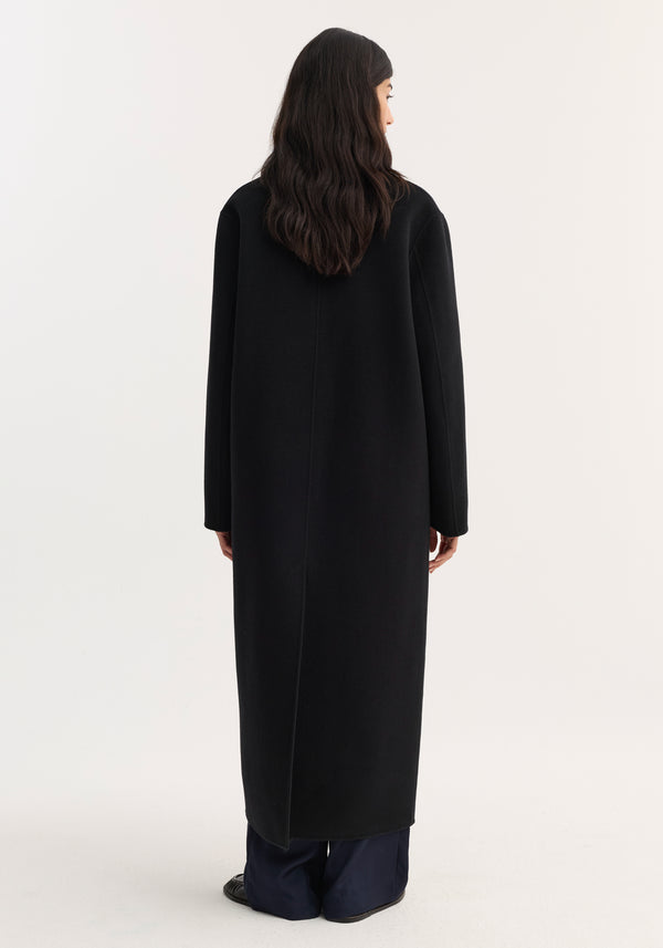 Woman wearing a Double-faced coat | black, showcasing its long, straight-cut silhouette and discreet side pockets, paired with wide-leg pants and black shoes.