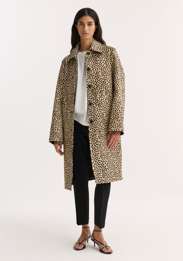 Model in a cheetah-print pony hair coat with leather-knotted buttons, white top, black trousers, and strappy sandals. The coat features hidden pockets and a structured silhouette.