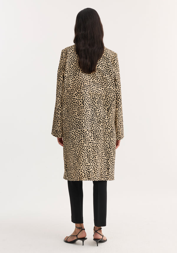 Back-view of a model wearing a knee-length Pony hair coat in cheetah print with leather button closures, over slim black trousers and strappy heeled sandals.