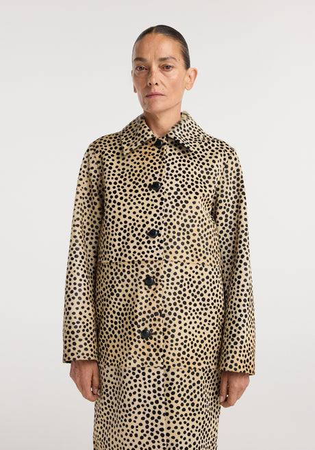 Woman wearing a long pony hair coat | cheetah with black spots on a tan background, paired with black pants, white top, and black strappy heels, standing against a white backdrop.