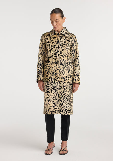 Woman wearing a long pony hair coat | cheetah with black spots on a tan background, paired with black pants, white top, and black strappy heels, standing against a white backdrop.