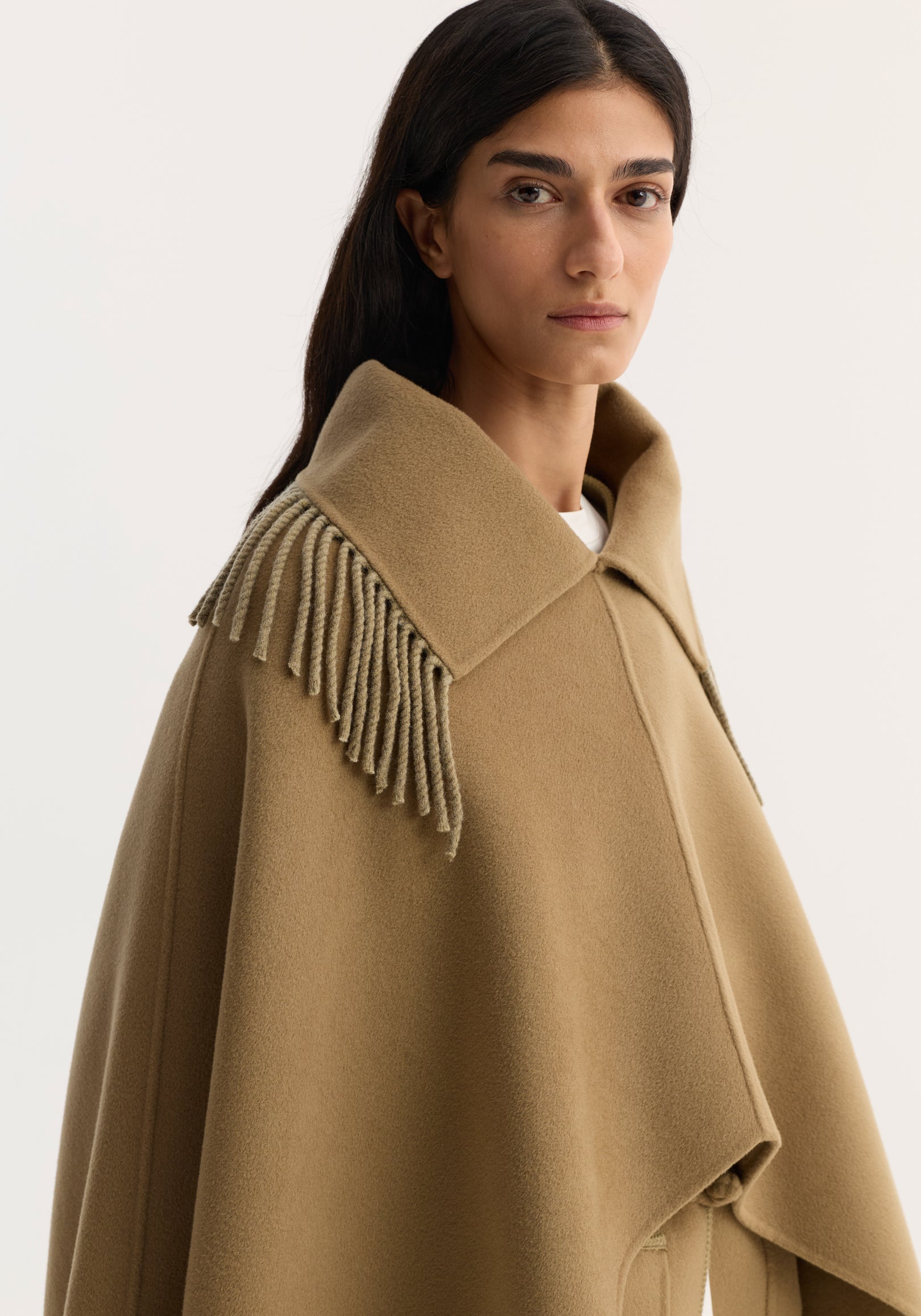 Model wearing Fringe scarf poncho in camel, featuring a wide collar, short fringe detailing, and an open poncho design made from a wool-cashmere blend.