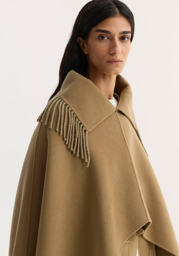 Model wearing Fringe scarf poncho in camel, featuring a wide collar, short fringe detailing, and an open poncho design made from a wool-cashmere blend.