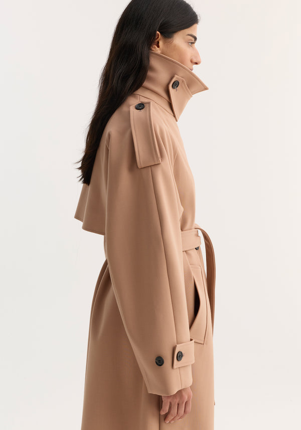 Woman in profile wearing an Oversized classic trench | powder, featuring a high collar, shoulder epaulettes, self-tie belt, and clean, minimalist design.