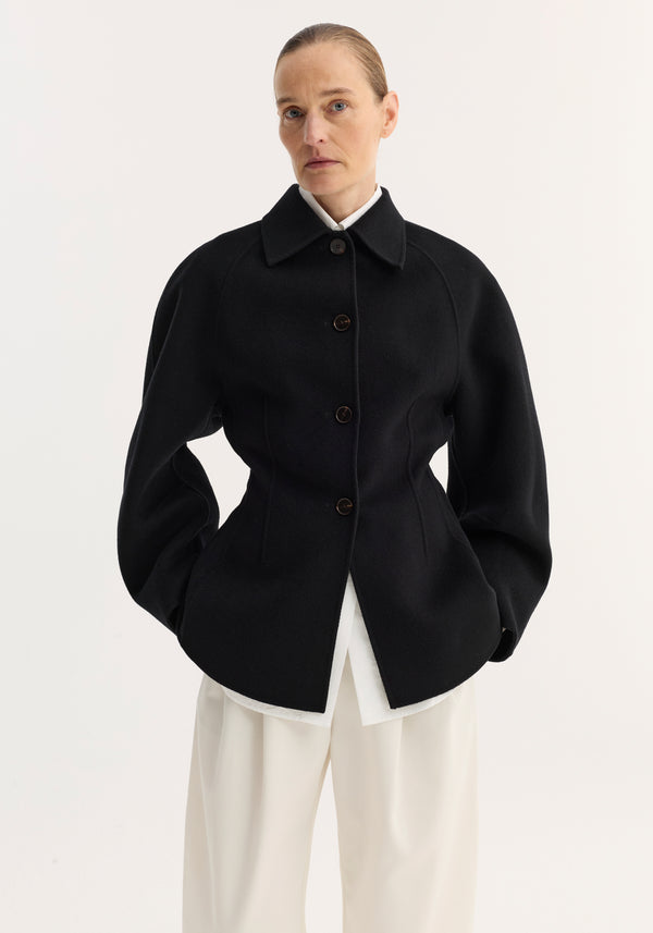 Model wearing a Double-faced sculptural jacket in black, featuring oversized sleeves, cinched waist, and four buttons, paired with wide-leg trousers.