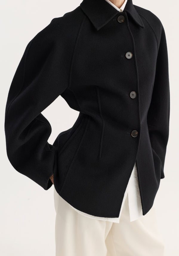 Torso view of a tailored Double-faced sculptural jacket in black, featuring oversized sculptural sleeves, a cinched waist, and four large dark button closures.