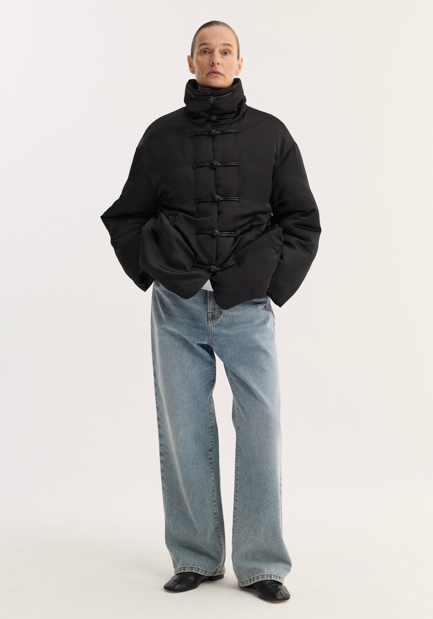 Padded puffer jacket | black with high collar, pankou closures, slanted pockets; model wears it with loose-fit jeans and low-heeled shoes.