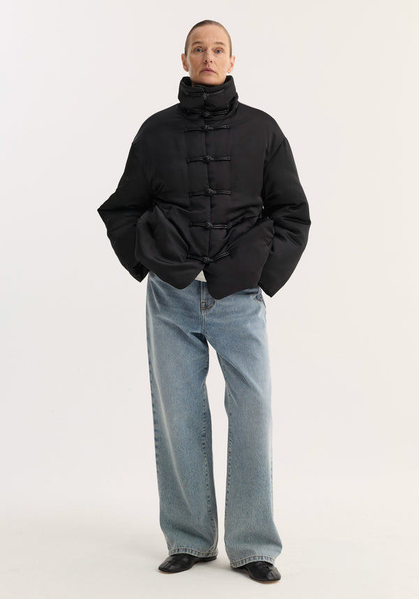 Padded puffer jacket | black with high collar, pankou closures, slanted pockets; model wears it with loose-fit jeans and low-heeled shoes.