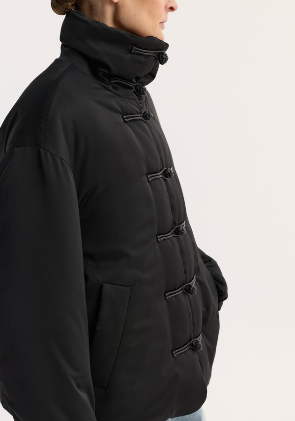 Padded puffer jacket | black, featuring quilt-style design, tall collar, pankou closures, and slanted welt pockets, worn with light-wash jeans.