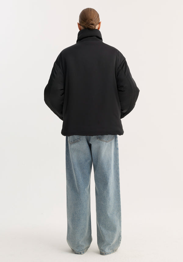 Person wearing a black padded puffer jacket with high collar, pankou closures, and slanted pockets, styled with light-wash wide-leg jeans.