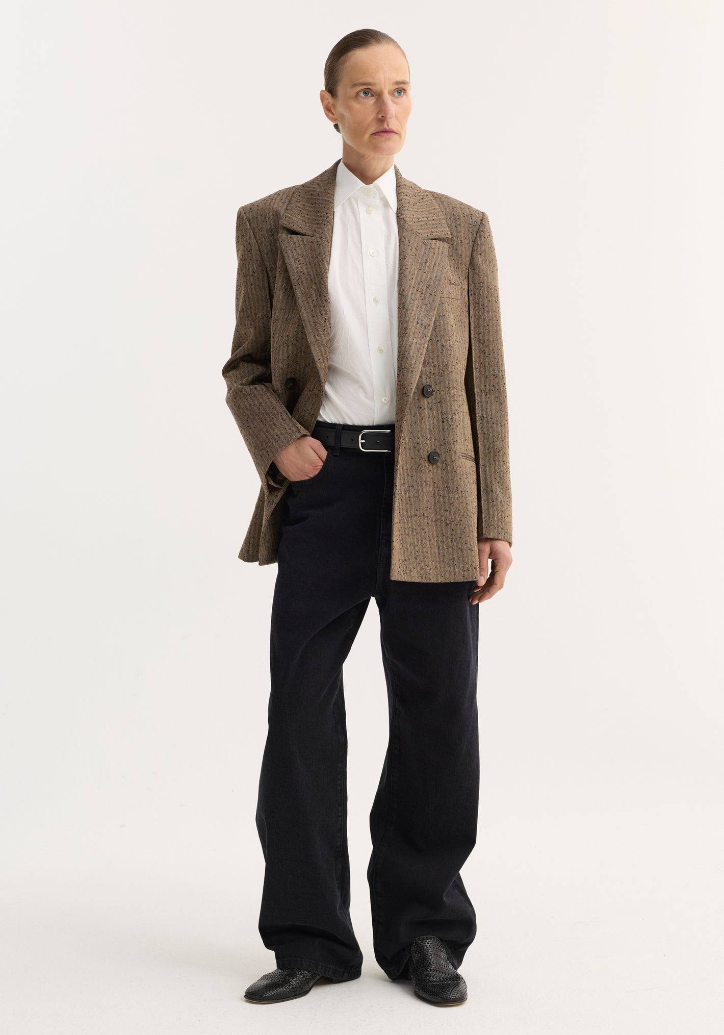 Model wearing a Double-breasted blazer | herringbone, featuring a tailored shoulder, chest pocket, and welt pockets, paired with black wide-leg trousers and slip-on shoes.