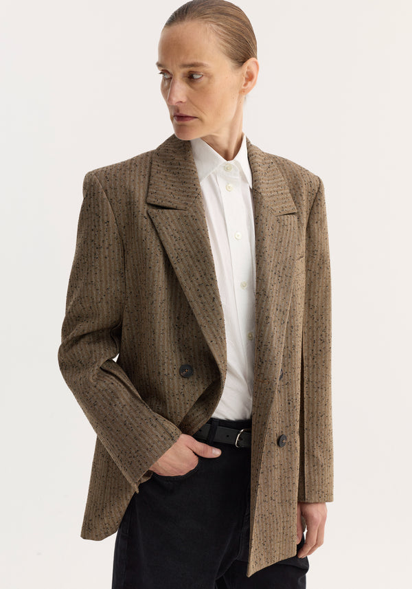 Person wearing a double breasted blazer | herringbone with welt and chest pockets, over a white shirt, hand in pocket, looking sideways.