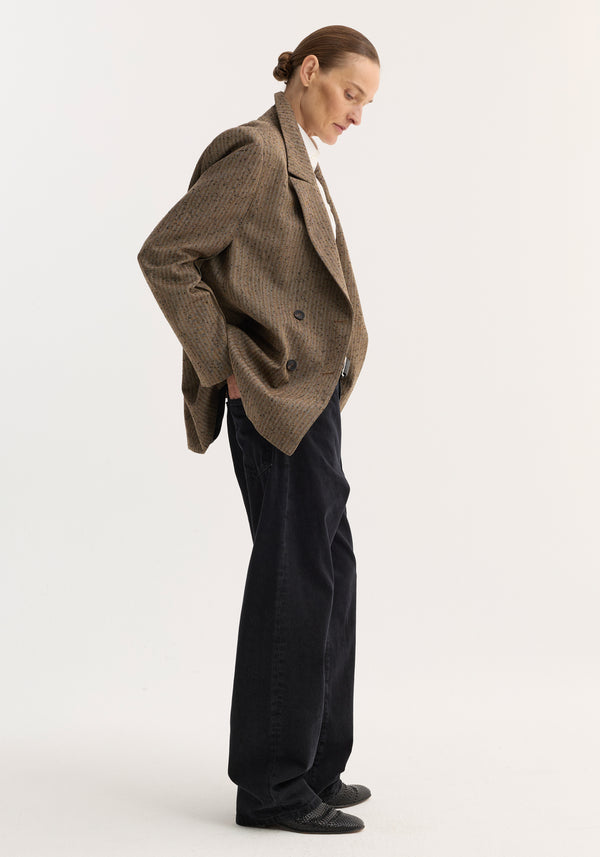 Side-profile view of a person wearing a Double breasted blazer | herringbone, showcasing its wide lapels and tailored silhouette, paired with loose black trousers.