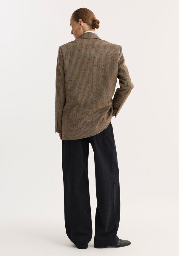 Person wearing a Double breasted blazer | herringbone with notched lapel, visible chest and welt pockets, paired with loose-cut black denim trousers.
