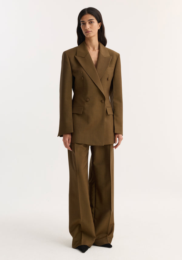 Model wearing Double-breasted waisted blazer in golden brown, featuring a sharp notch lapel, strong shoulders, and a structured, feminine silhouette against a plain background.