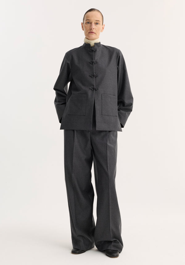 Model wearing the Mandarin jacket | dark grey melange, featuring a mandarin collar, pankou closure, and patch pockets, paired with matching trousers over black shoes.