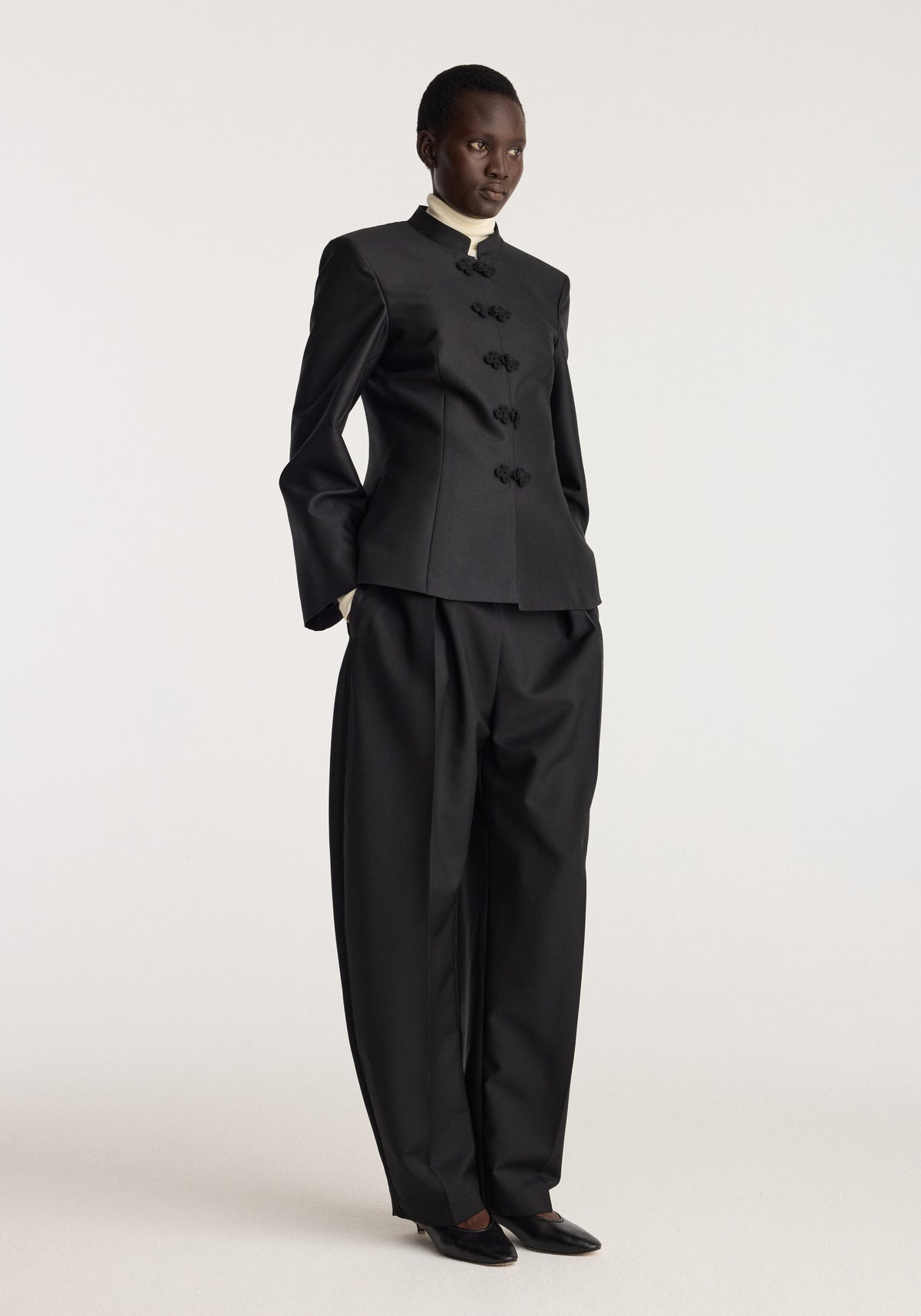 Sculptural pankou closure blazer | black shown on a model with Mandarin collar and button closures paired with wide leg black trousers in a studio setting