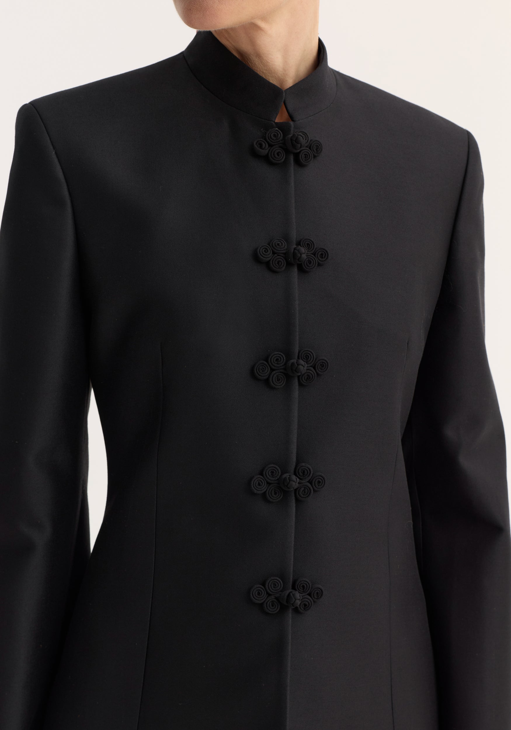 Sculptural mandarin blazer in black, showcasing a sleek, tailored fit with a high collar and decorative frog closures, crafted from a wool-silk blend.