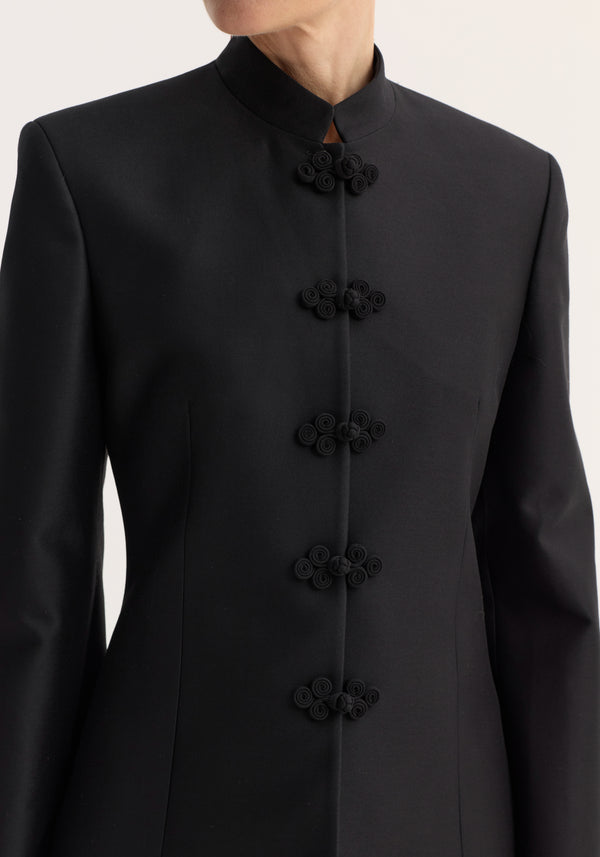 Sculptural mandarin blazer in black, showcasing a sleek, tailored fit with a high collar and decorative frog closures, crafted from a wool-silk blend.