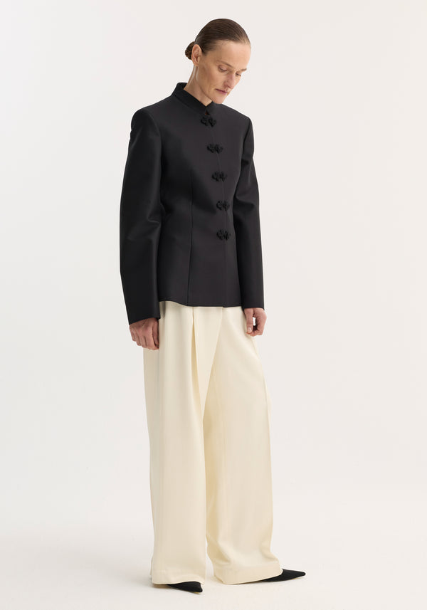 Model in Sculptural mandarin blazer, black, with fitted waist and pankou closures, paired with wide-leg trousers and pointed shoes, showcasing modern tailoring.