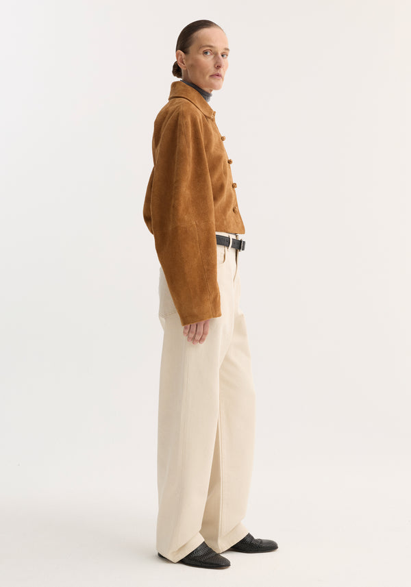Woman in profile wearing the Rounded textured suede jacket in cognac, showcasing its cropped fit, knotted leather buttons, and structured sleeves over a slim turtleneck.