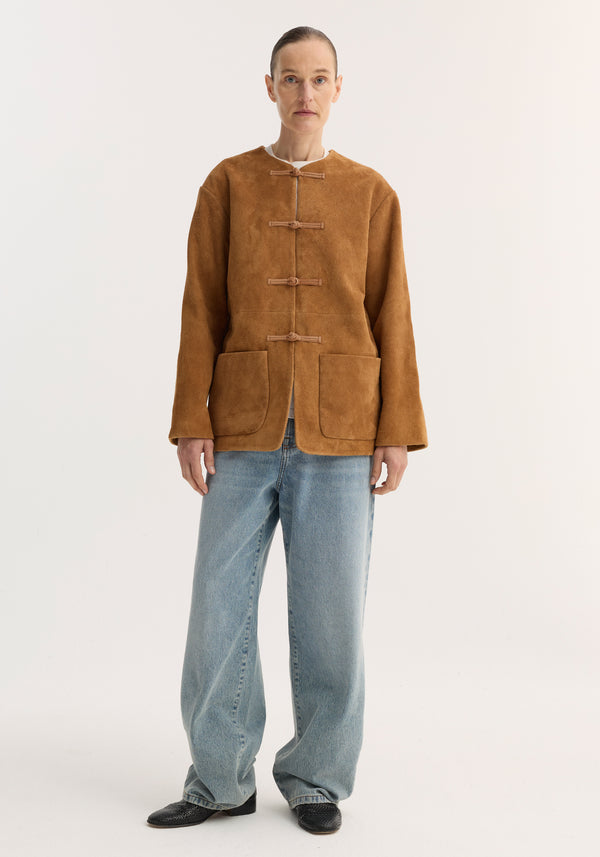 Model wears the Mandarin textured suede jacket in cognac, featuring pankou closures and patch pockets, paired with loose light-wash jeans and black slip-on shoes.