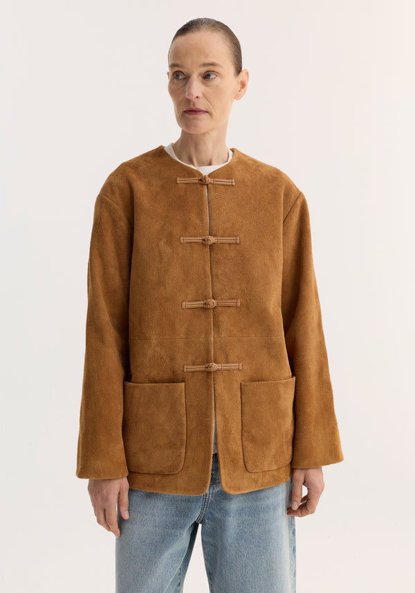 Model wearing the Mandarin textured suede jacket | cognac, featuring pankou closures, embroidered edges, and patch pockets, styled with a white top and light-wash jeans.