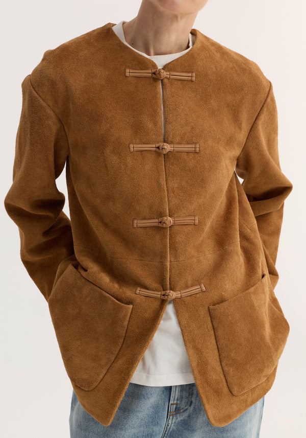 Mandarin textured suede jacket | cognac features pankou closures, embroidered edges, and large patch pockets. Model wears it over a white T-shirt with jeans.