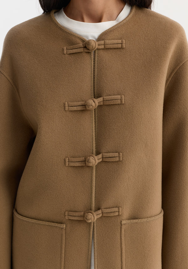 Mandarin double-faced wool jacket in camel with pankou closures, embroidered edges, and patch pockets. White shirt peeks out at the collar.