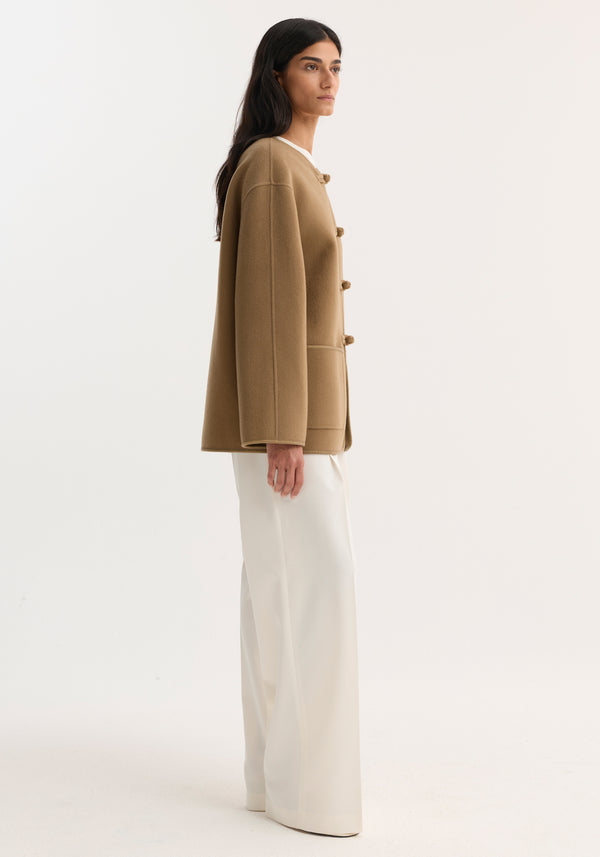 Mandarin double-faced wool jacket with toggle-style fastenings, embroidered edges, and patch pockets, paired with wide-leg trousers, side-profile shot against a light background.