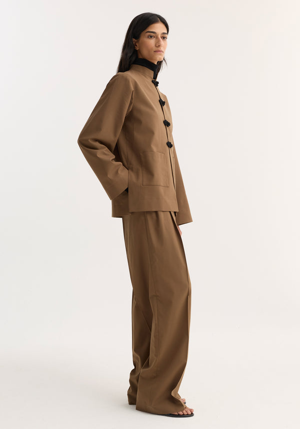 Model in profile wearing Mandarin Jacket | mocha, with pankou closures, wide sleeves, and patch pockets, paired with matching wide-leg trousers and minimalist sandals.