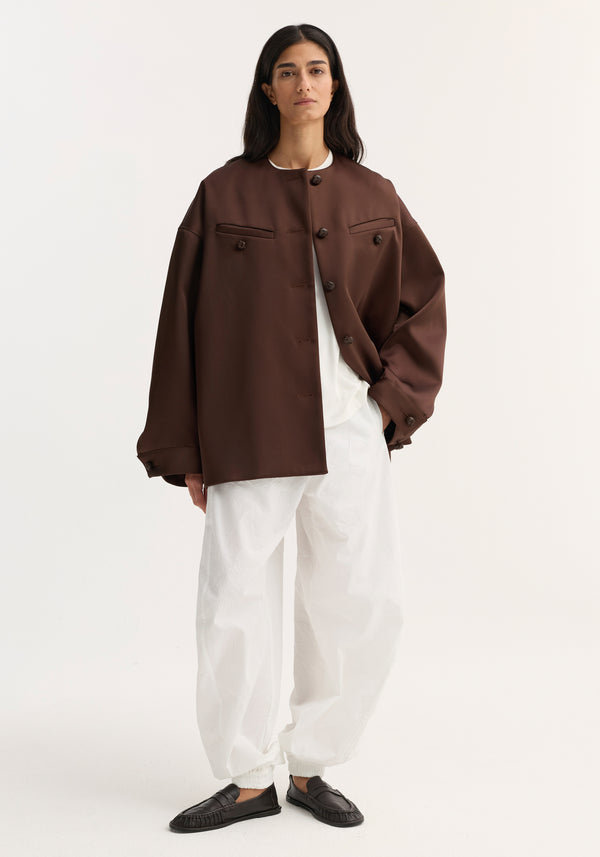 Model wearing the Western heavy satin jacket in espresso with leather-knotted buttons, over a white top and trousers, styled with dark loafers.