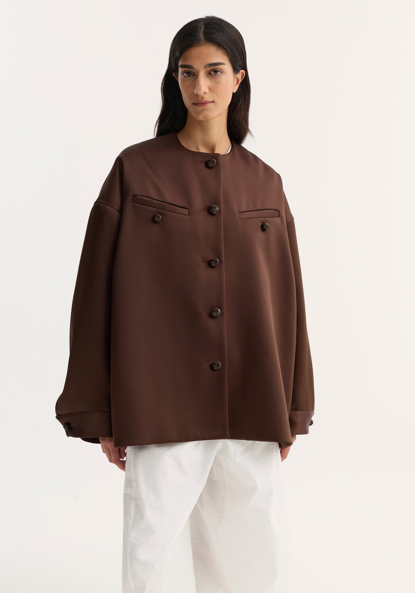 Model in Western heavy satin jacket | espresso, featuring oversized fit, leather-knotted buttons, chest welt pockets, paired with wide-leg trousers for a minimalist style.