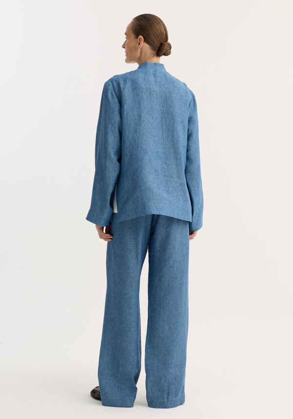 Back view of a woman wearing the Mandarin jacket in ocean blue, featuring pankou closures, embroidered edges, and patch pockets. Her hair is in a neat bun.