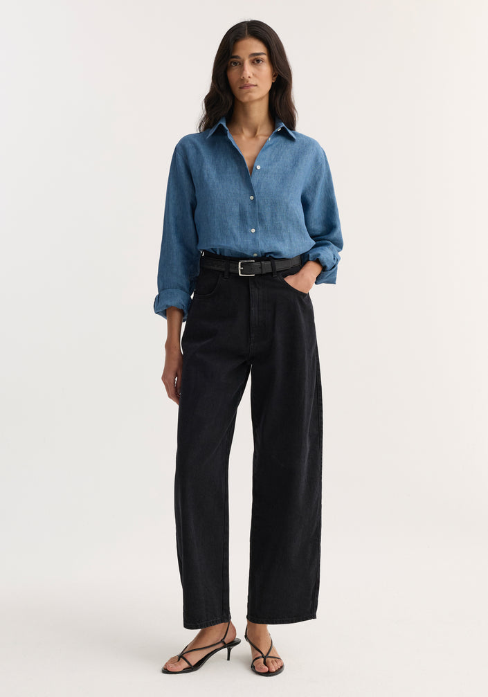 Woman wearing Barrel leg denim | black jeans with wide-leg silhouette, tucked denim shirt, and strappy sandals, showcasing the contemporary barrel-leg style and heritage details.