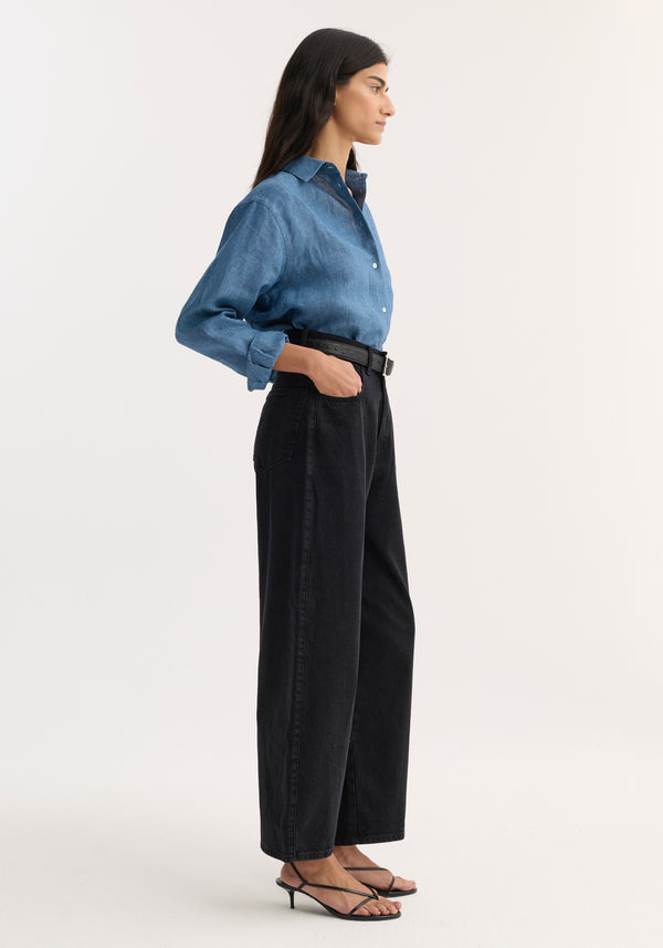 Model wearing Barrel leg denim | black, showcasing high-waisted, wide-leg jeans with a black belt, paired with a chambray shirt and strappy sandals.