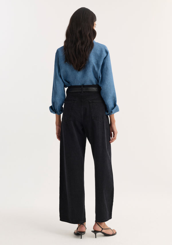 Back view of Barrel leg denim in black, featuring wide-leg, high-waisted cut with heritage details, paired with a chambray shirt and strappy sandals.