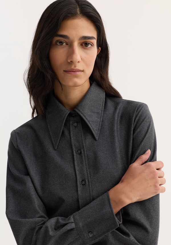 Person wearing a fitted shirt in dark grey melange, featuring a sharp pointed collar and button-down front, crafted from lightweight virgin wool flannel.