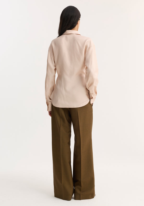 Back view of a person wearing a Silk Shaped Shirt in rose, featuring a relaxed fit, button-down front, and rounded hem, paired with wide-leg trousers.