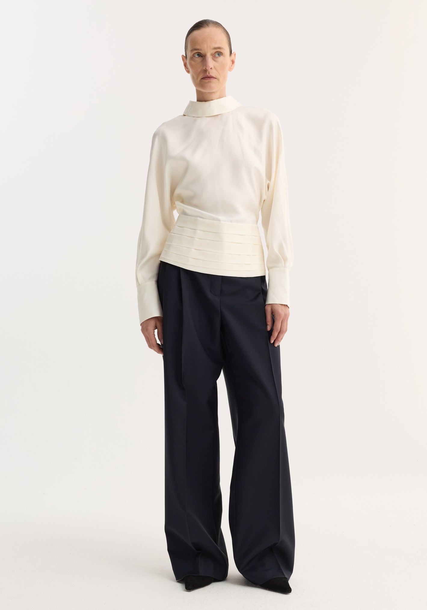 Tuxedo silk top | cream, with a high-neck, voluminous sleeves, cummerbund waist, and dramatic open-back slit, paired with wide-leg trousers.