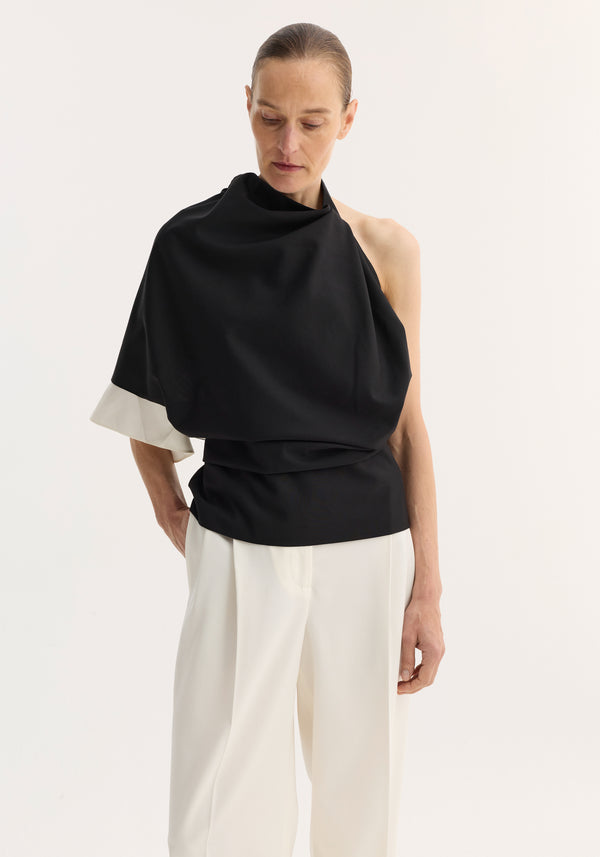 Model wearing Draped open back wool top, featuring an asymmetric design with a single sleeve and wrap waist, paired with wide-leg high-waisted trousers.