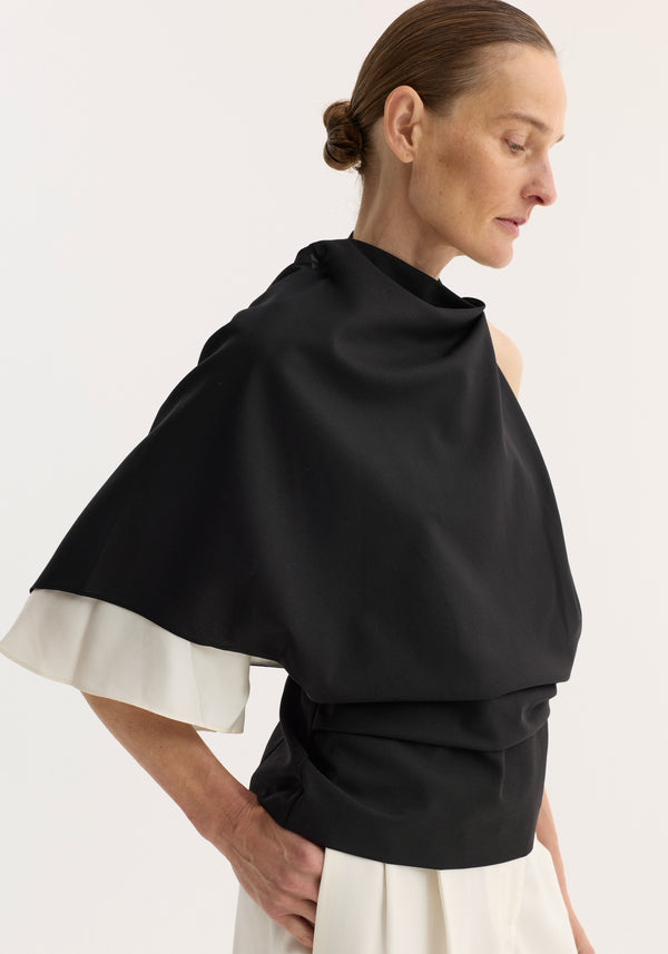 Model in profile wearing Draped open back wool top | black, featuring a sculptural, one-shoulder design with a single sleeve and contrasting silk insert.