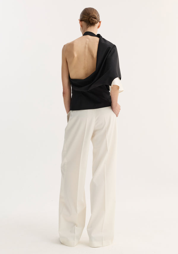Model in Draped open back wool top showcasing its wrap design and asymmetric single sleeve, paired with high-waisted trousers, emphasizing a minimalist, fashion-forward style.