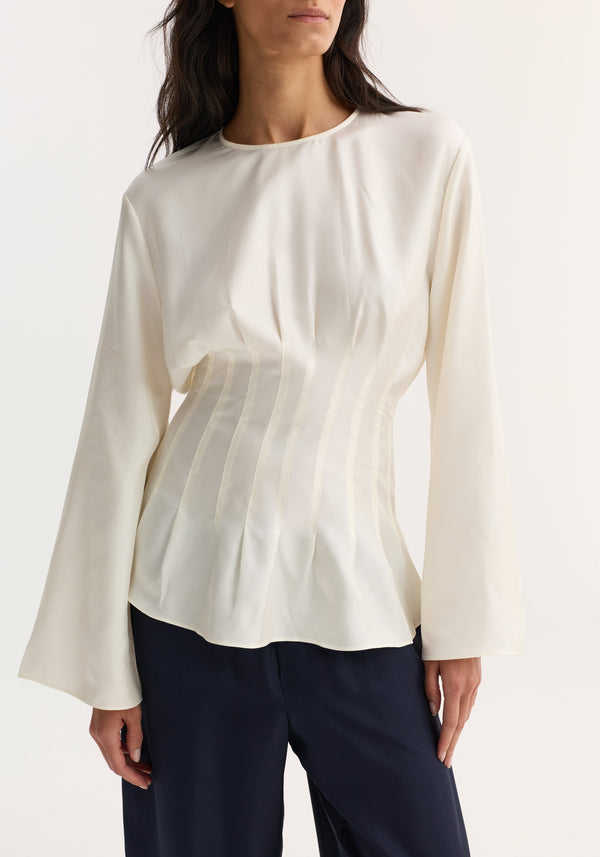 Pleated silk top in cream with long sleeves, a softly structured waist, and a back keyhole closure, paired with navy-blue trousers for an elegant look.