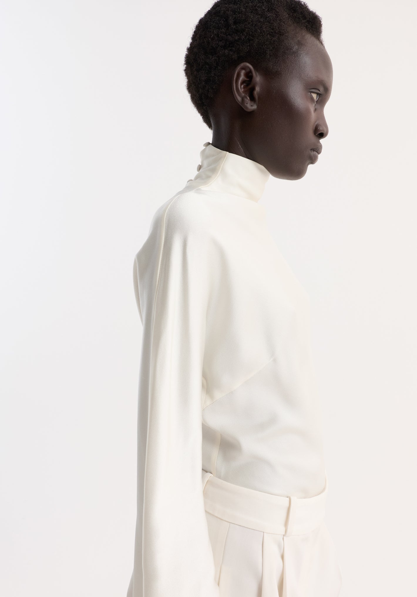 Model in Satin Waisted Top | cream, showcasing a high-neck, fluid satin blouse with draped sleeves and button closures, paired with matching high-waisted trousers.
