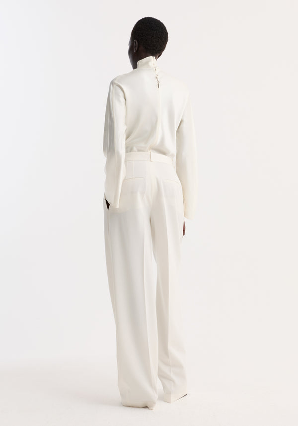 Person in a sleek Satin Waisted Top | Cream, featuring long sleeves, a high mandarin collar, and delicate buttons down the back, paired with wide-leg trousers.