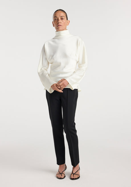 Person wearing Satin waisted top | cream in a sleek, long-sleeve design with a high neckline paired with black slim trousers and black strappy heels against a plain background.