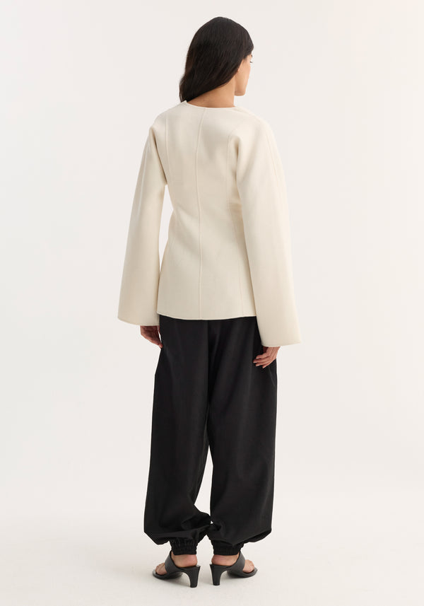 Model wearing the Sculptural long sleeve top with voluminous sleeves, defined waist, and V-neckline, paired with black jogger pants and open-toe heels.