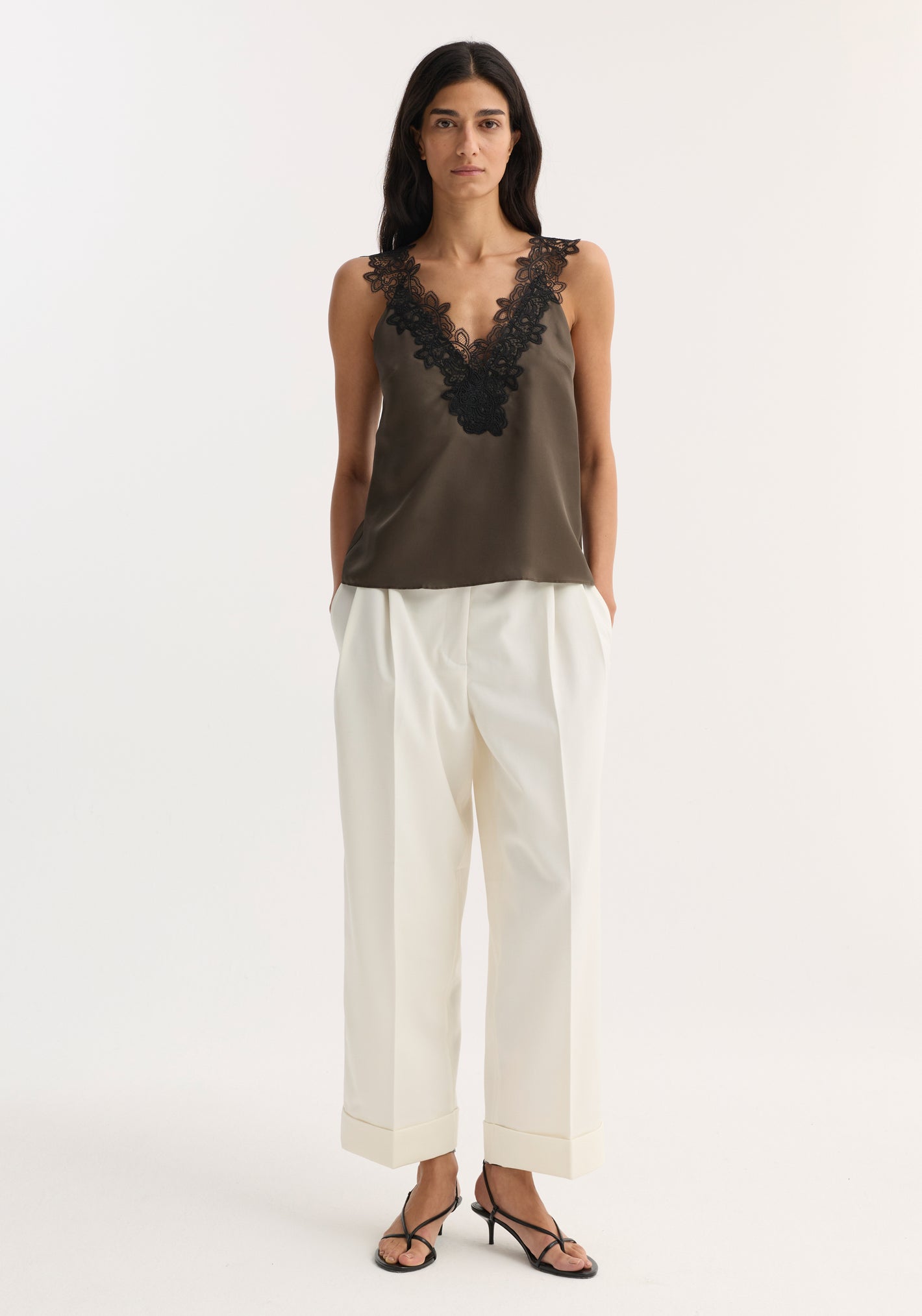 Woman wearing V-neck silk lace top | earth, with deep V-neck and black lace, paired with high-waisted wide-leg trousers and heeled sandals.
