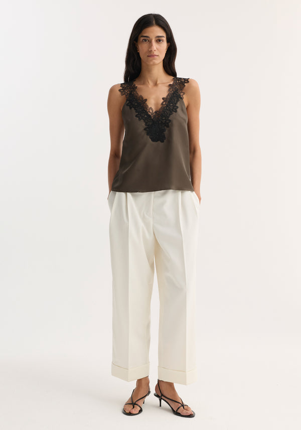 Woman wearing V-neck silk lace top | earth, with deep V-neck and black lace, paired with high-waisted wide-leg trousers and heeled sandals.